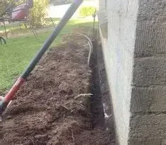 Freshly dug soil trench next to home foundation for termite treatment.