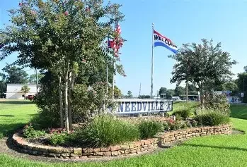 Needville welcome sign with flags and trees, representing local service coverage.