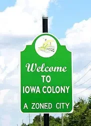 Iowa Colony welcome sign under blue sky, representing local service coverage.